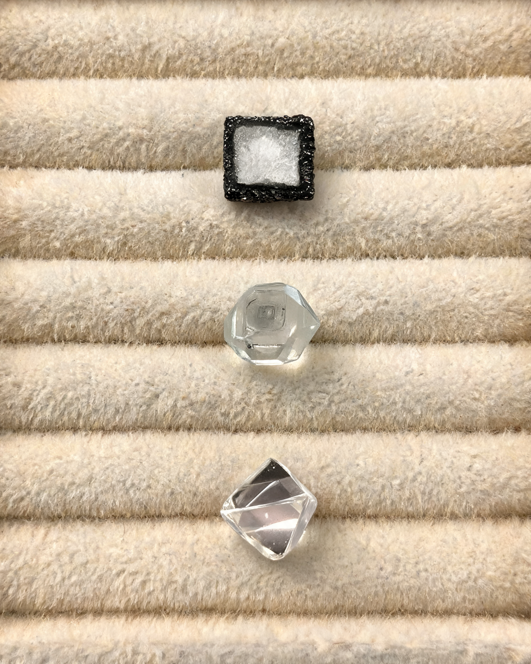 Three diamond roughs arranged on a jeweler's tray. Top: Chemical Vapor Deposition rough; middle: High Pressure High Temperature rough; bottom, a natural mined diamond rough.